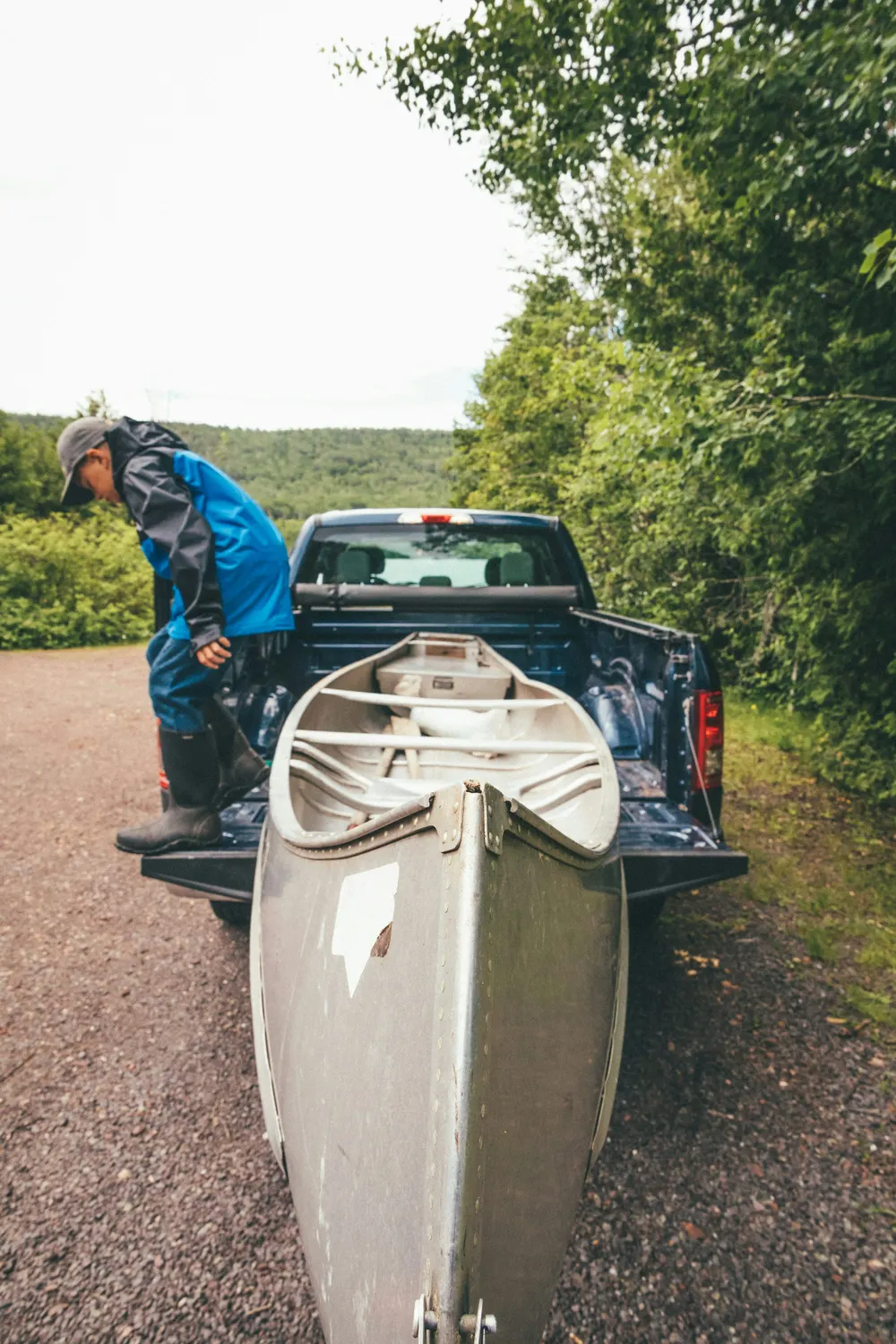 Paddler lifting a white canoe off the back of a pickup truck at a forest access point