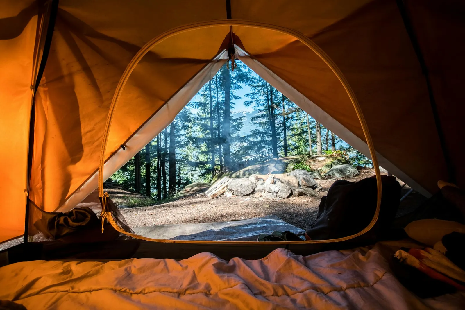 View from inside an open orange tent looking out at a sunny forest campsite