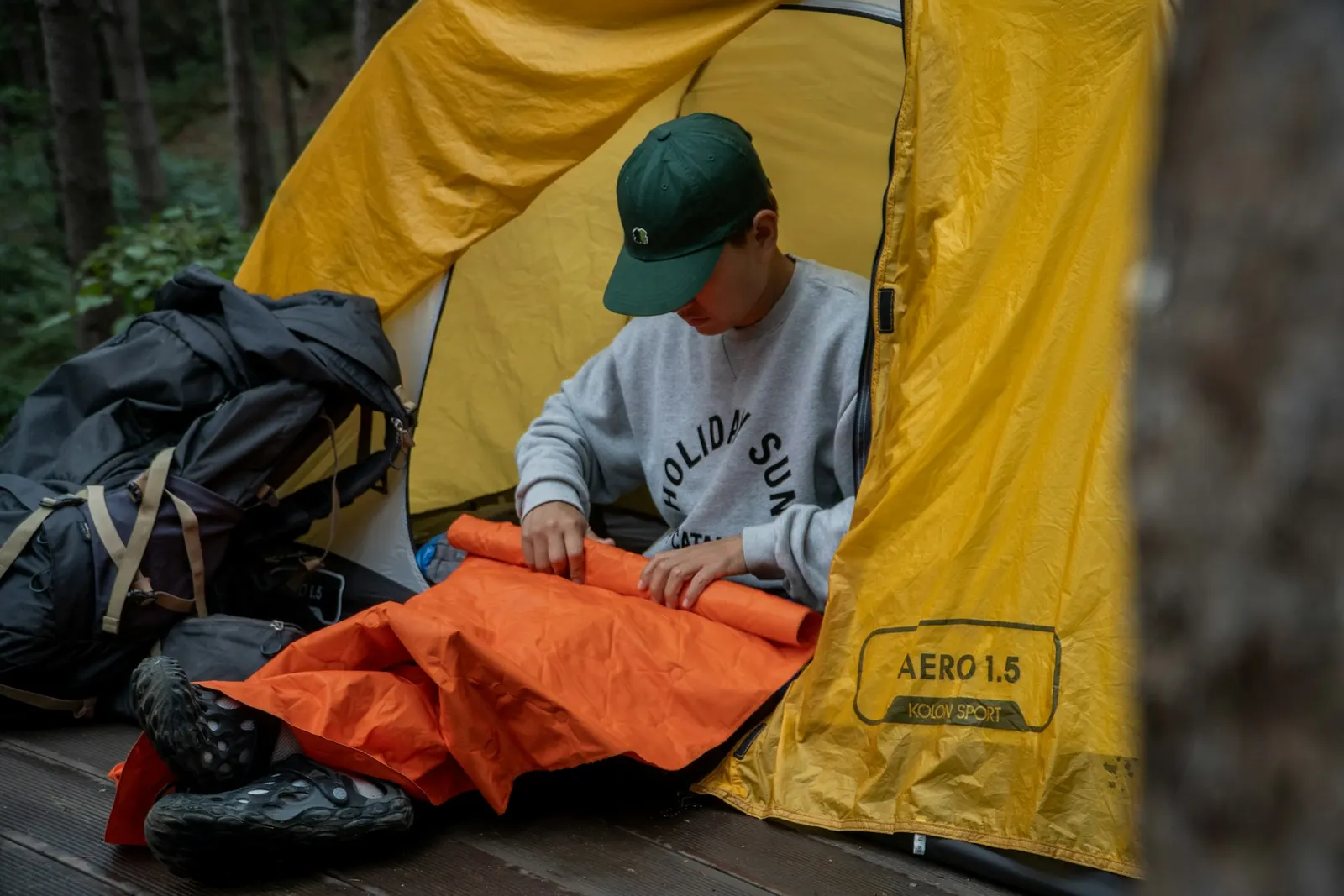 Camper inside a yellow tent laying out an orange sleeping bag on a pad