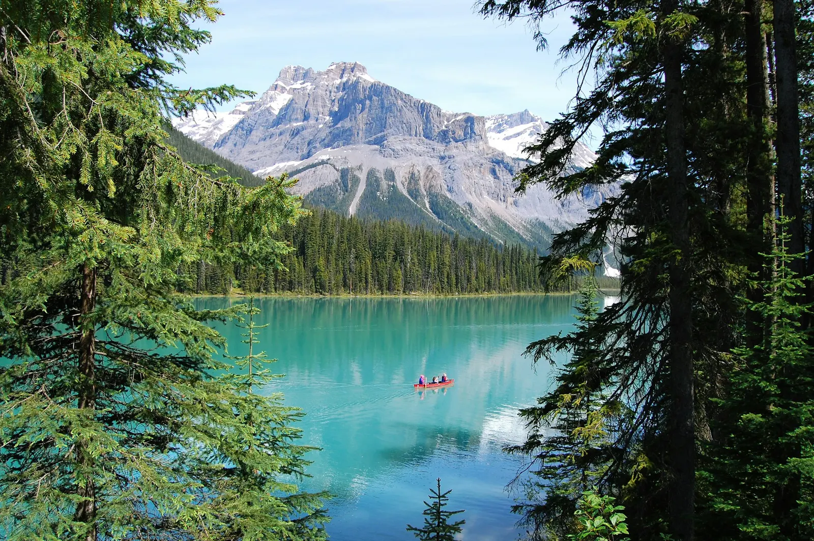 Red canoe on a turquoise mountain lake framed by tall pine trees and peaks