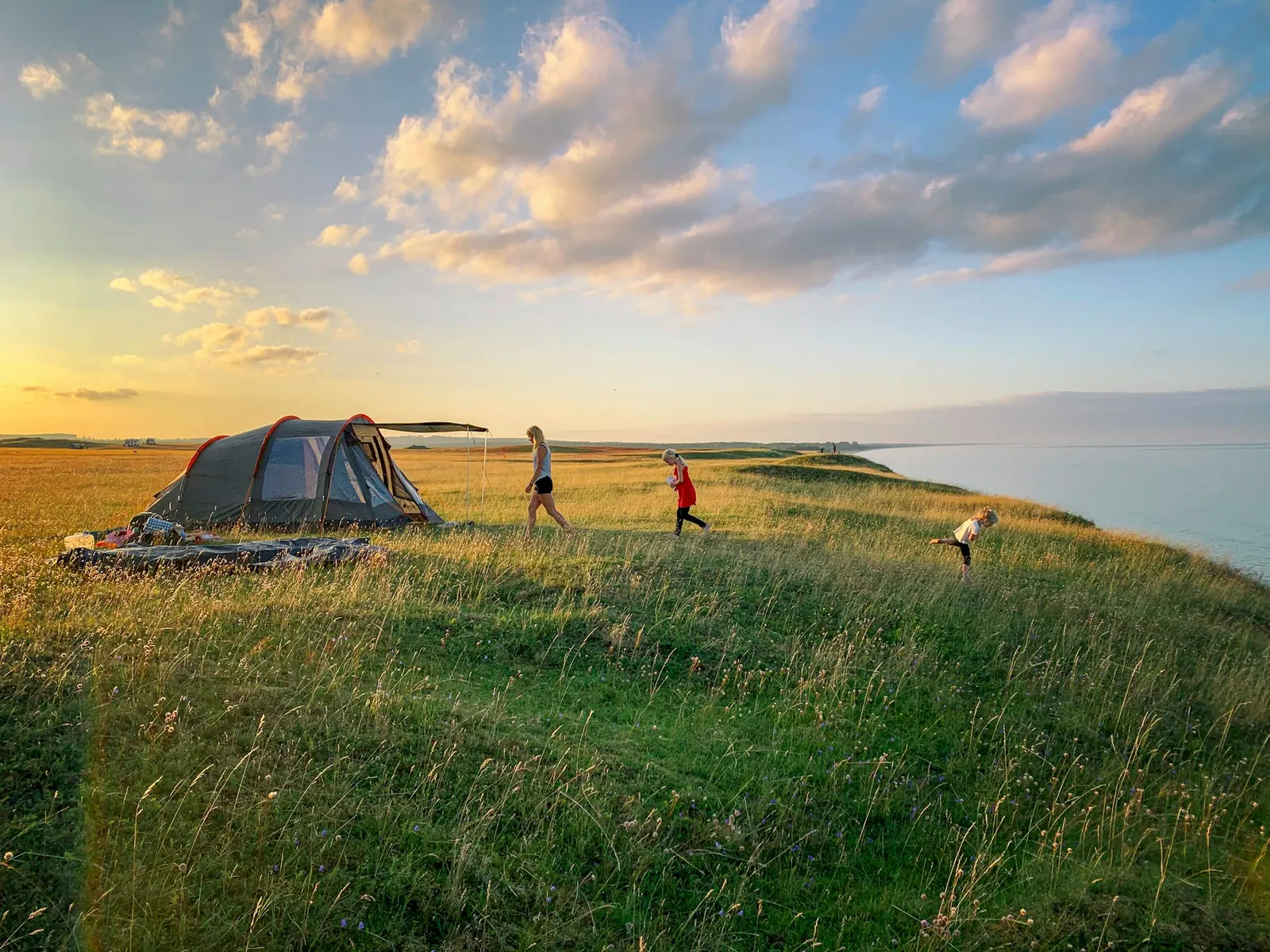 Family tent on a grassy campsite by the water at sunset with children running nearby